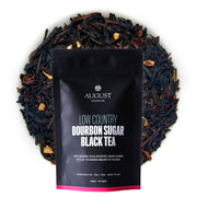 Black tea package labeled 'August' surrounded by loose leaf tea on a white background