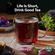 Clear mug of tea with flowers and text 'Life Is Short, Drink Good Tea' on a wooden table.