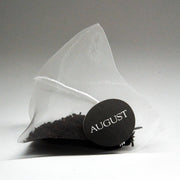 Tea bag with a black label reading 'August' on a gray background