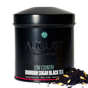 Black tea canister with 'August' branding and tea leaves on a white background
