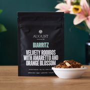 August Biarritz tea package with a bowl of tea leaves on a wooden surface.