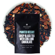 August tea bag with 'Painted Desert' description surrounded by tea leaves on a white background