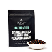 Black tea package labeled 'August' with a bowl of tea leaves on a white background