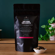 Black tea package with visible text on a wooden surface with a green plant in the background