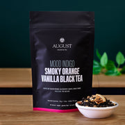 August tea package with a small bowl of tea leaves on a wooden surface