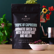 August tea package with a bowl of tea leaves on a wooden surface