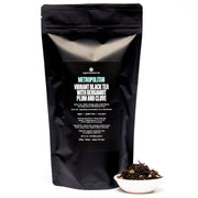 Black tea package with visible text and a small bowl of tea leaves on a white background