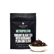 Black tea package with 'August Uncommon Tea' branding and a bowl of tea leaves on a white background