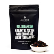 Black tea package with 'August' branding and tea leaves in a bowl on a white background