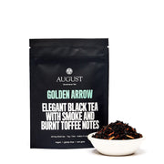 Black tea package labeled 'August' with a bowl of tea leaves on a white background
