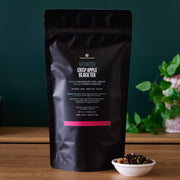 Black tea package with a small bowl of tea leaves on a wooden surface