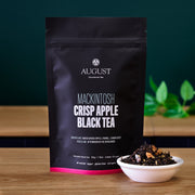 August tea package with a bowl of black tea leaves on a wooden surface