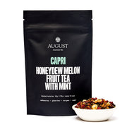 Black tea packaging labeled 'August Capri Honeydew Melon Fruit Tea with Mint' next to a bowl of tea.