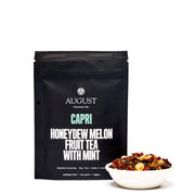 August Capri honeydew melon fruit tea with mint packaging and tea leaves in a bowl on a white background