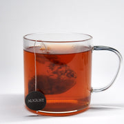 Clear glass mug with red tea and a visible 'August' brand label on a white background
