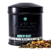 Black tea canister with 'August' branding and tea leaves on a white background