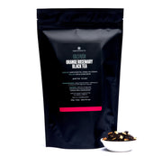 Black tea packaging with visible text and a small bowl of tea leaves on a white background