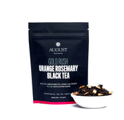 August Gold Rush Orange Rosemary Black Tea package with tea leaves in a bowl on a white background