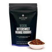 August Negroni Bittersweet Orange Rooibos tea package with a bowl of tea leaves on a white background