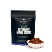 August Negroni Bittersweet Orange Rooibos packaging with a small bowl of tea leaves on a white background