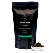 Black tea packaging with a small bowl of tea leaves on a white background