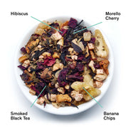 Assorted dried tea leaves including hibiscus, morello cherry, smoked black tea, and banana chips on a white plate.