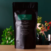 Black tea packaging labeled 'Rare Leaves' on a wooden surface with a green background and plants.