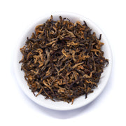 Dry black tea leaves in a white bowl on a white background