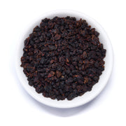 Dark brown tea leaves in a white bowl on a white background