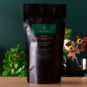 Black coffee packaging with 'Rare Leaves' branding on a wooden surface with plants and flowers in the background.