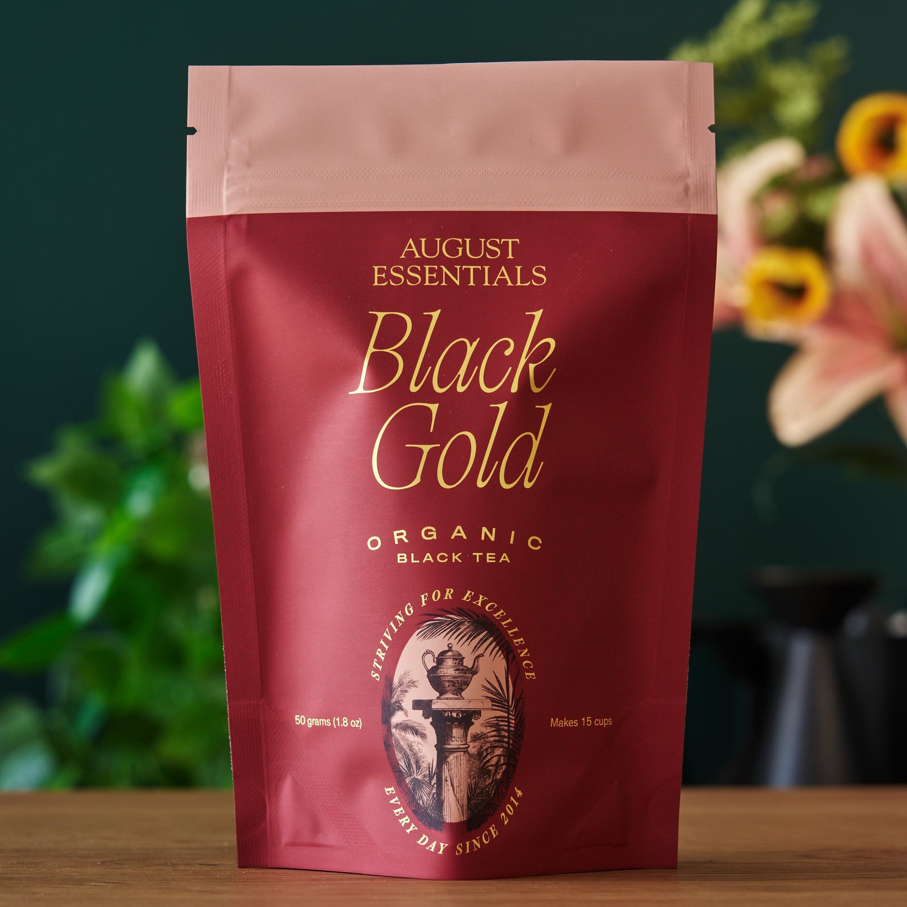 August Essentials Black Gold Organic Black Tea package on a wooden surface with a blurred background