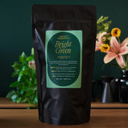 Black tea package with green label on a wooden surface with plants and flowers in the background