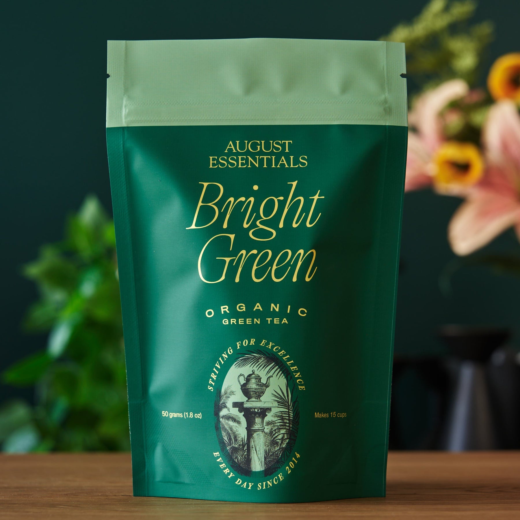 Green tea package with 'August Essentials Bright Green' branding on a wooden surface.