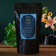 Black tea package with a blue label on a wooden surface with plants in the background