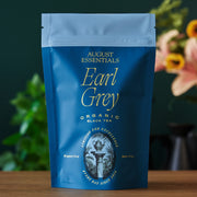 Blue package of August Essentials Earl Grey Organic Black Tea on a wooden surface with a blurred background
