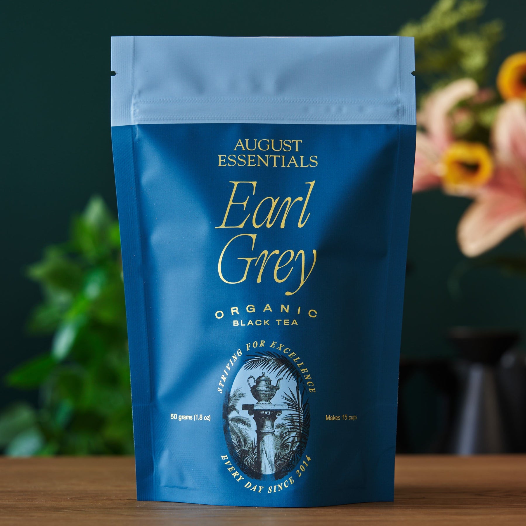 Blue package of August Essentials Earl Grey Organic Black Tea on a wooden surface with a blurred background