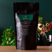 Black tea packaging labeled 'Rare Leaves' on a wooden surface with a green background and plants.