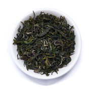 Dry green tea leaves in a white bowl on a white background