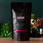 Black tea package with visible branding on a wooden surface with decorative plants in the background