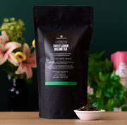 Black tea package with 'Superbloom' branding on a wooden surface with flowers in the background