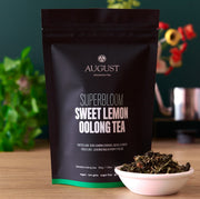 August Superbloom Sweet Lemon Oolong Tea package with tea leaves in a bowl on a wooden surface.