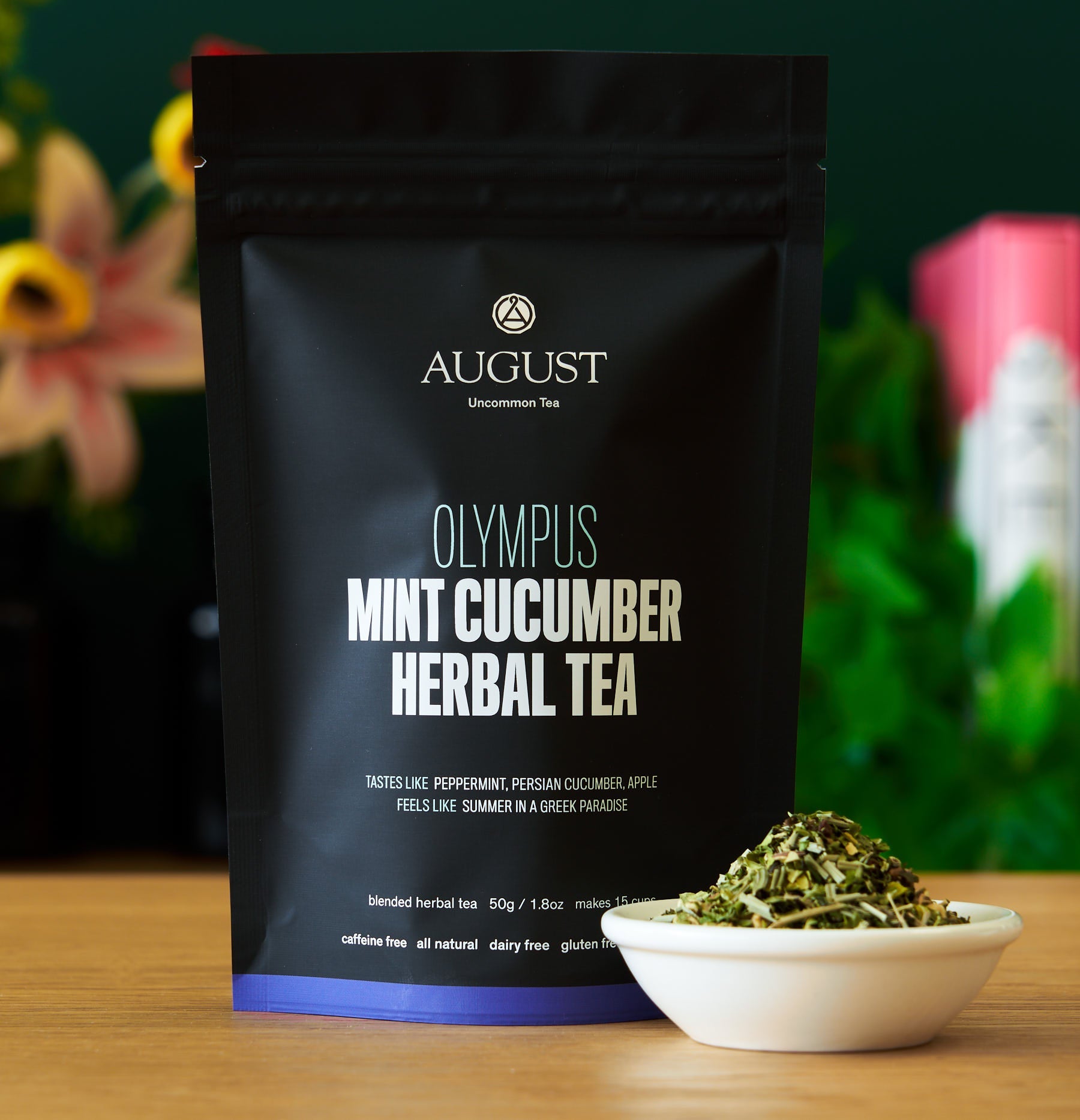 August Olympus Mint Cucumber Herbal Tea package with tea leaves in a bowl on a wooden surface.