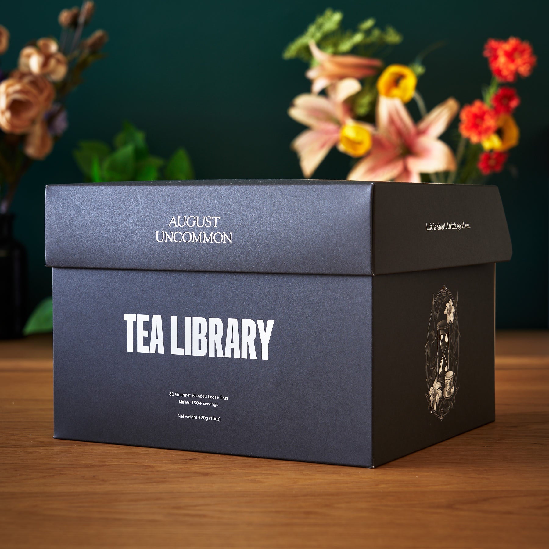 Tea library box with 'August Uncommon' branding on a wooden surface with flowers in the background