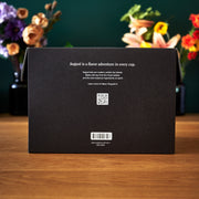 Black box with text and barcodes on a wooden surface with flowers in the background