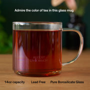 Clear glass mug with tea on a wooden surface, featuring branding text.