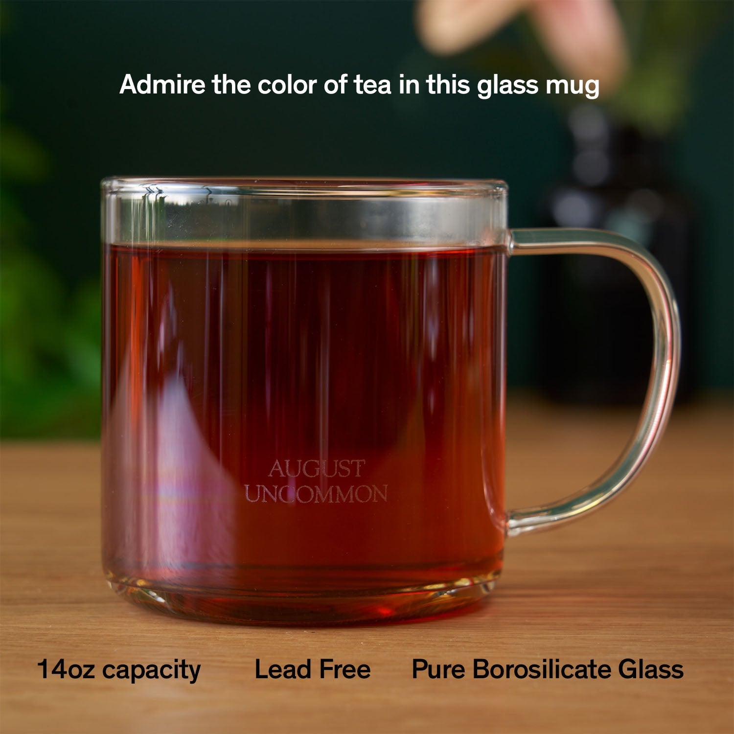 Clear glass mug with tea on a wooden surface, featuring branding text.
