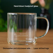 Clear glass mug with handle on a wooden surface, featuring text about material and safety.