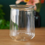 Clear glass jar with 'August Uncommon' branding on a wooden surface with a blurred background