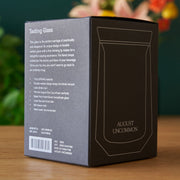 Box of August Uncommon tasting glass with product details on a wooden surface.