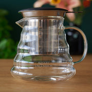 Clear glass coffee maker with metal filter on a wooden surface